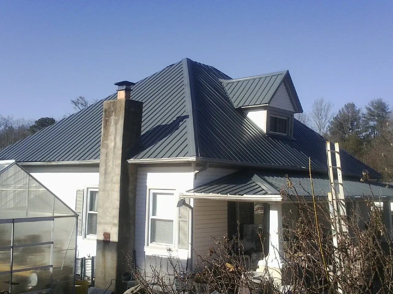 Dark blue standing seam metal roof on a white farmhouse with dormer — Slate & Tile Roof Repair by Roofing Brothers in Hopkins
