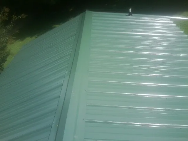 New green metal panels meeting at the ridge of a roof — Flat Roof Repair work by our crew in Hopkins