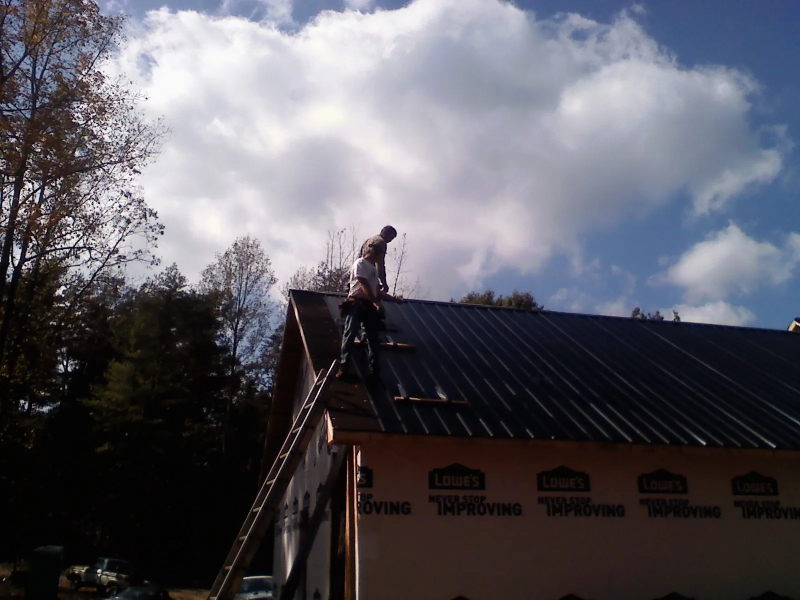 Roofer fastening dark metal panels high against a cloudy sky, from a Roof Inspection job in Hopkins
