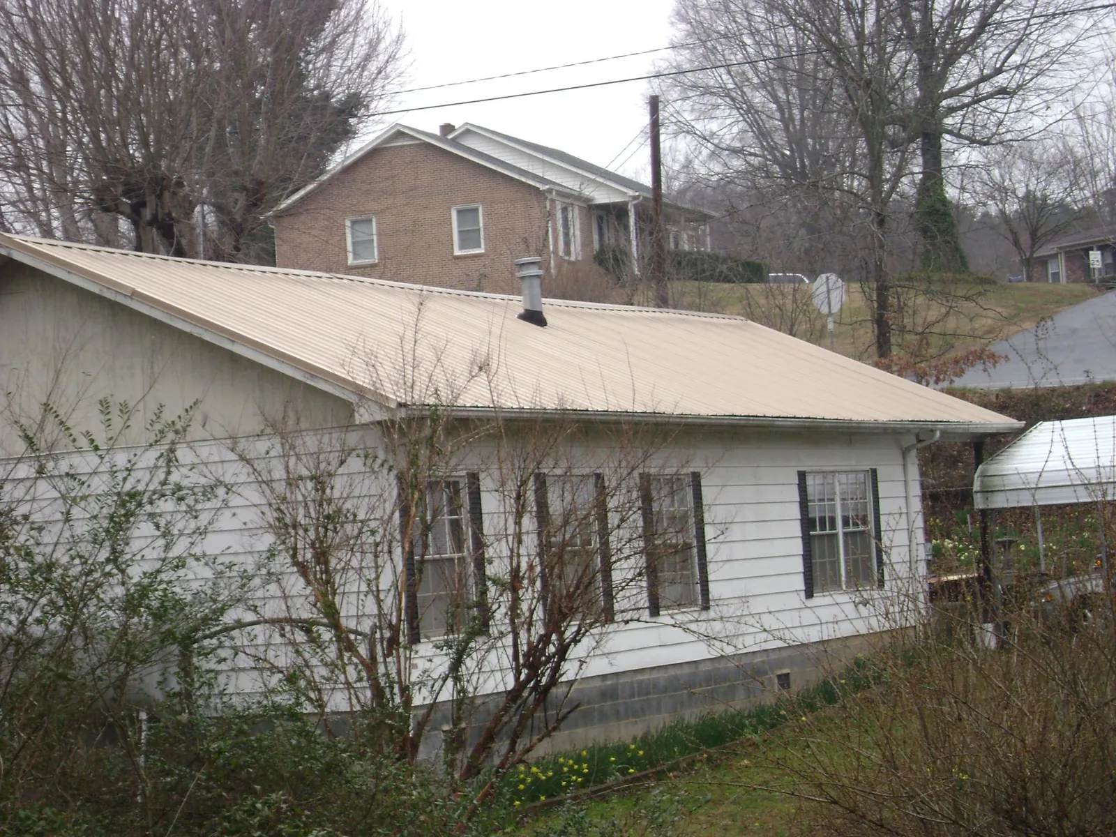 Tan metal roof on a white sided house set into a hillside — Commercial Roofing by Roofing Brothers in Hopkins